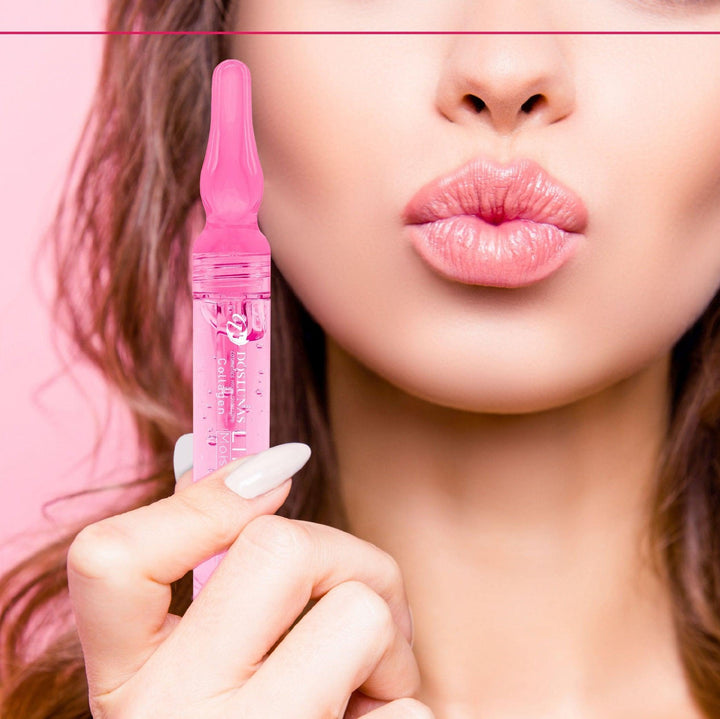 A small, white tube with a gold lid, labeled "Dos Lunas Collagen Lip Serum Balm (5 mL)," sits on a white marble counter. A green plant and a pink makeup brush are placed beside it.